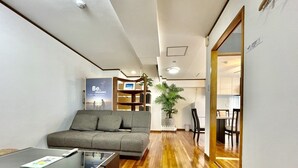 A modern living room with a grey sofa, a glass-top coffee table, a bookshelf, and a potted plant. - Hotel Umizola (Naha)