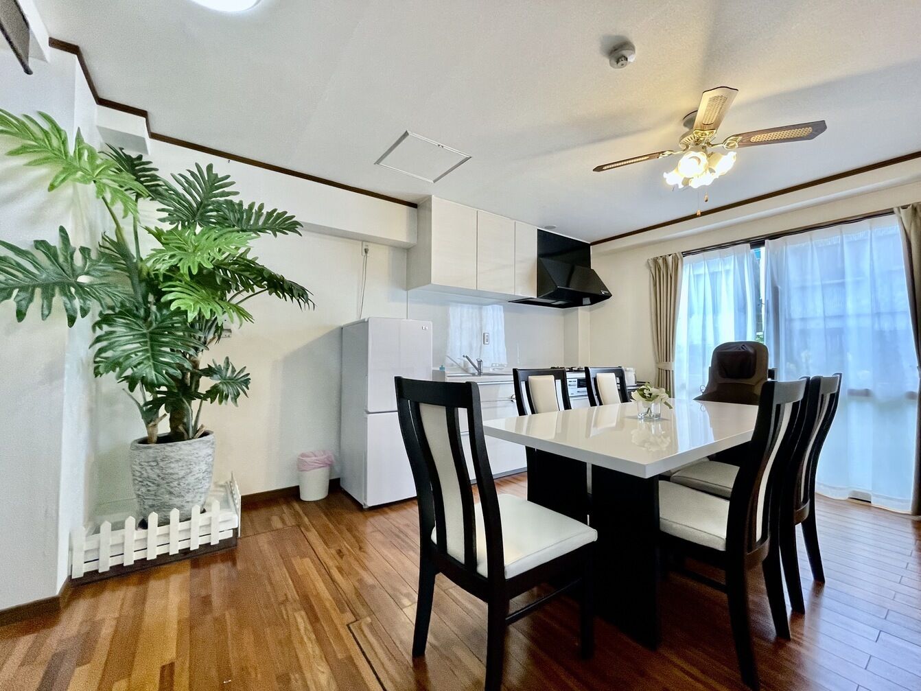 Una cocina moderna con armarios blancos, una mesa de comedor con sillas, un ventilador de techo y una planta en maceta.