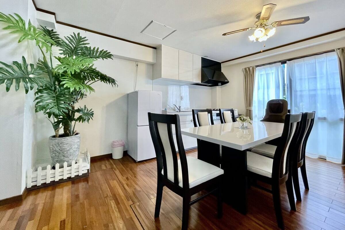 A modern kitchen with white cabinets, a dining table with chairs, a ceiling fan, and a potted plant.