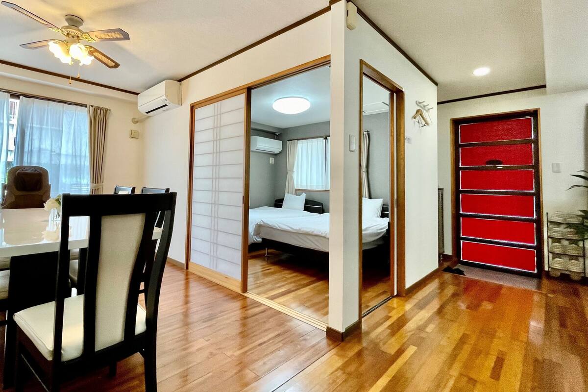 A room with a dining table, chairs, a bed, a red cabinet, and a ceiling fan.