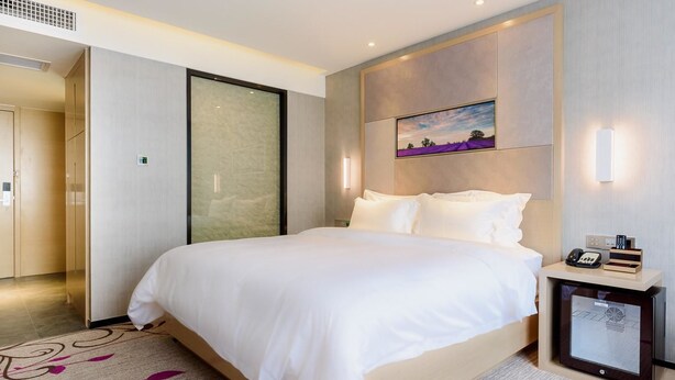 A modern hotel room with a large bed, a bedside table with a phone and a small screen, and a painting on the wall. - LAVANDE HOTEL GZ ZHENGJIA PLAZA BRANCH (Guangzhou)