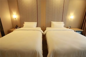 Une chambre d’hôtel avec deux lits simples, chacun doté d’une table de chevet et d’une lampe, ainsi qu’une petite table avec une lampe et un téléphone.