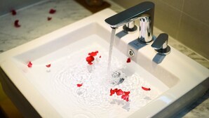 A bathroom sink with running water and rose petals. - LAVANDE HOTEL GZ ZHENGJIA PLAZA BRANCH (Guangzhou)