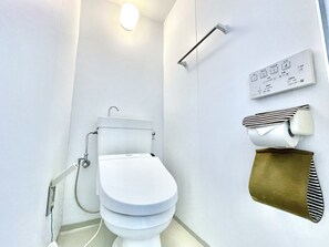 A modern bathroom with a toilet, a hand dryer, and a toilet paper holder. - Villa Izumizaki (Naha)