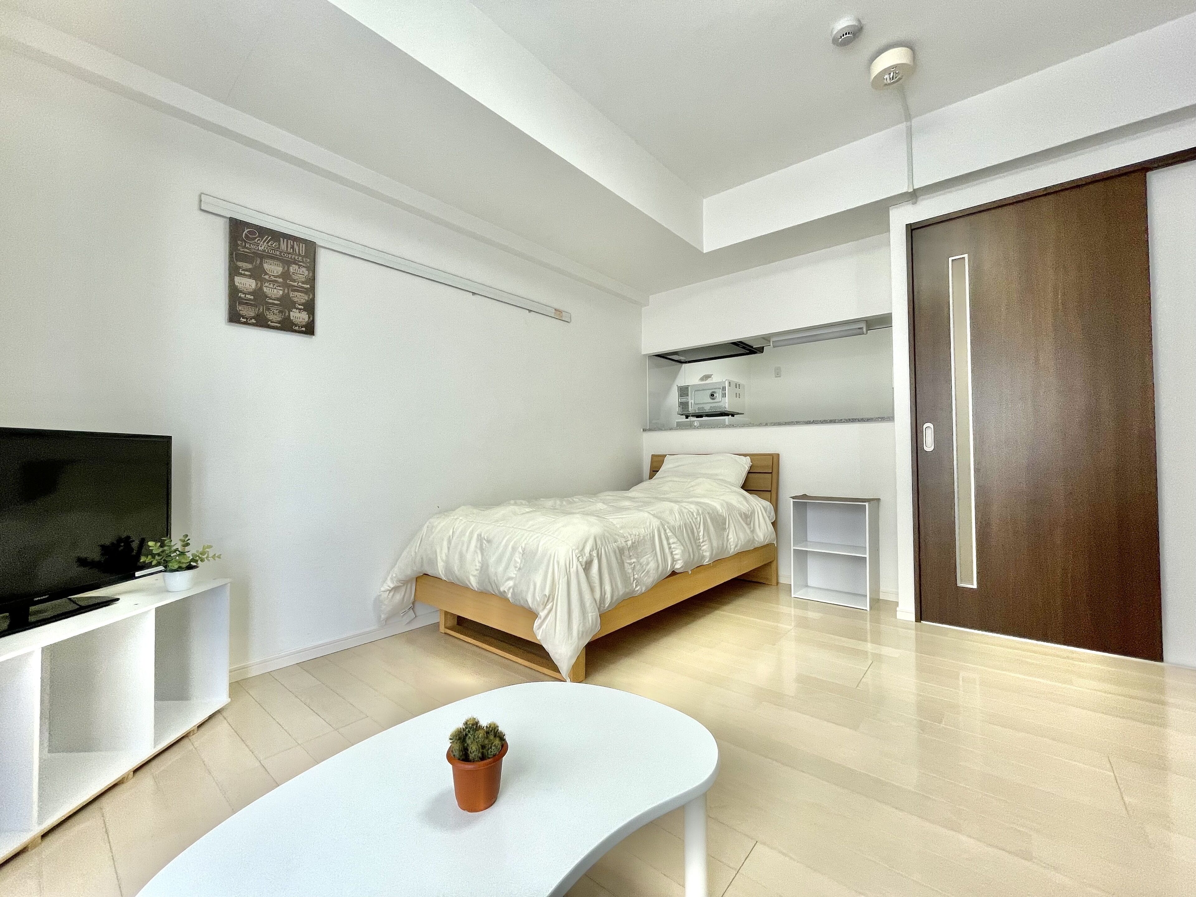 Quarto moderno com cama, televisão, mesa pequena e planta em vaso.