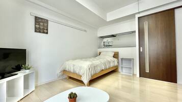 Quarto moderno com cama, televisão, mesa pequena e planta em vaso.