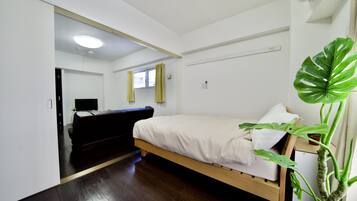 A bedroom with a bed, a TV, a plant, and a window with curtains.