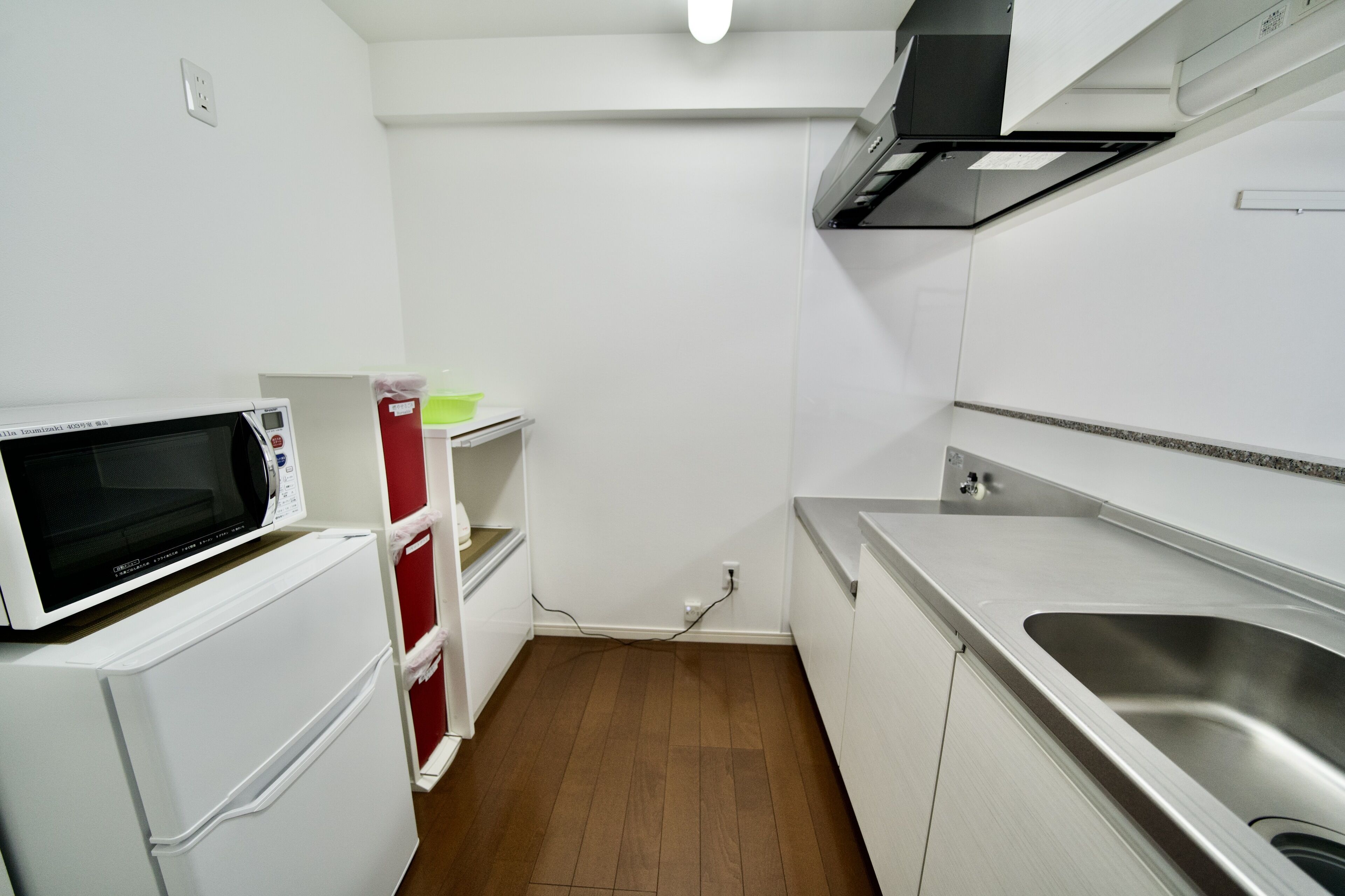 A compact kitchen with a microwave, refrigerator, and stainless steel sink.