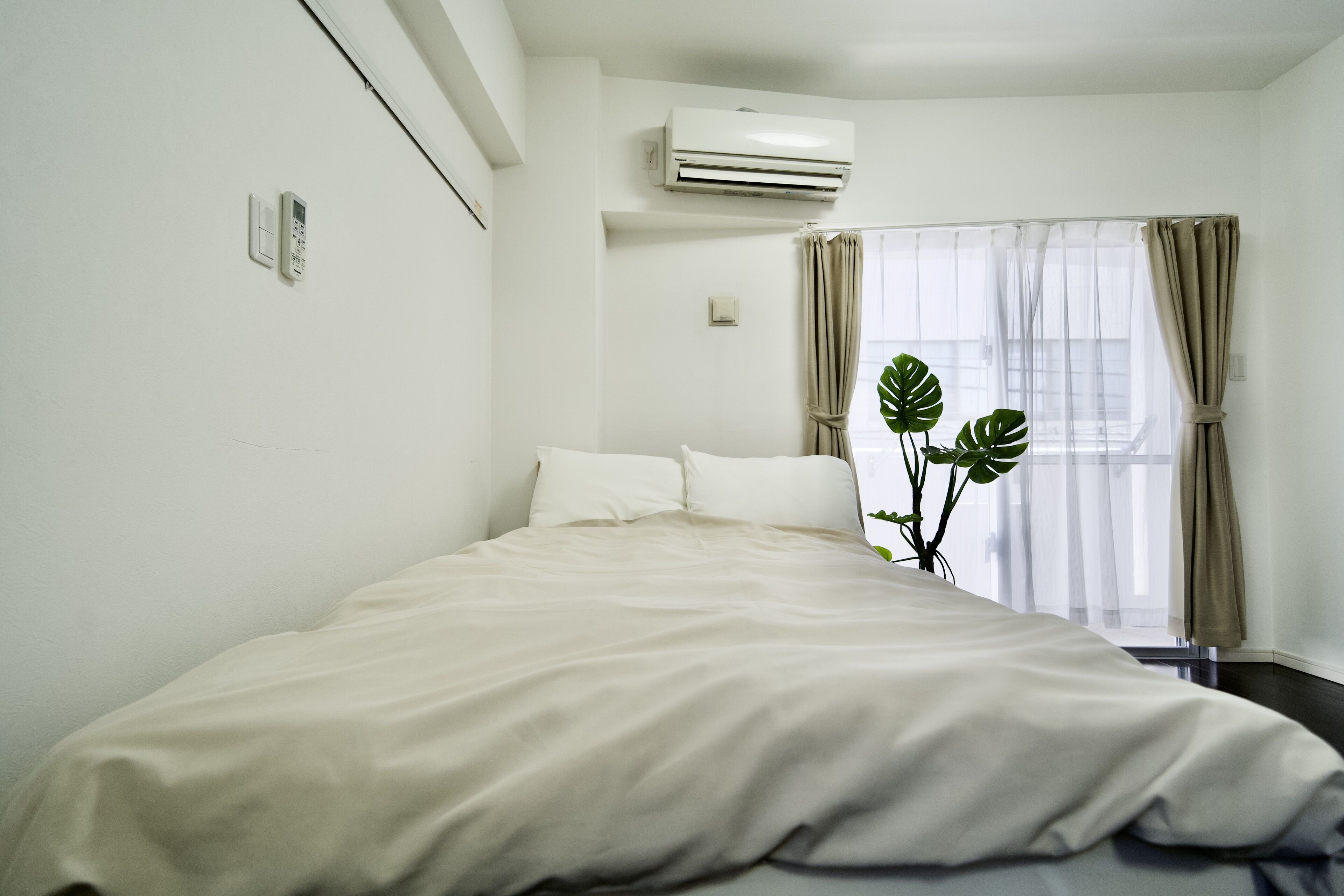 A hotel room with a bed, air conditioning unit, curtains, and a window with a plant.