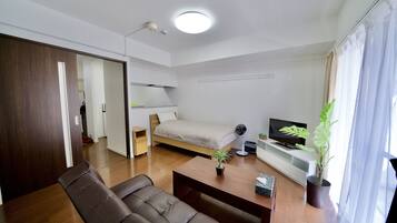 A modern, well-lit room with a bed, a desk, a chair, a TV, and a potted plant.