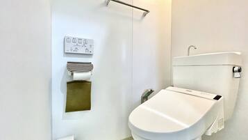 A modern bathroom with a toilet, a hand dryer, and a paper towel dispenser.