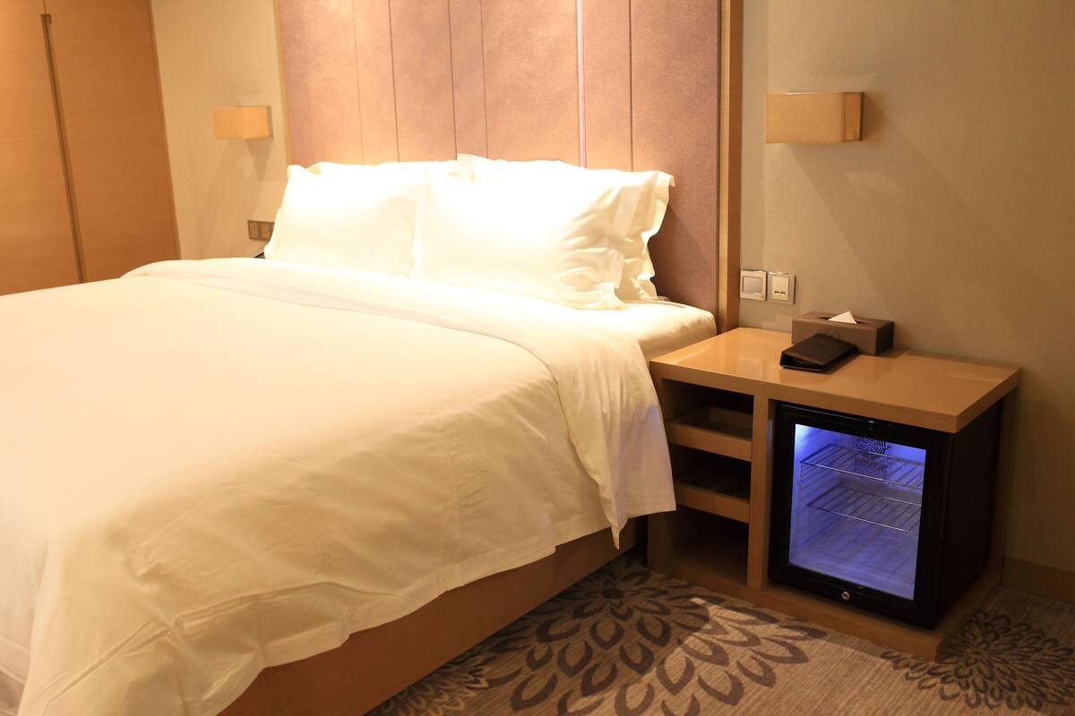 Ett hotellrum med en säng, sängbord, ett inbyggt minikylskåp och en mönstrad matta.