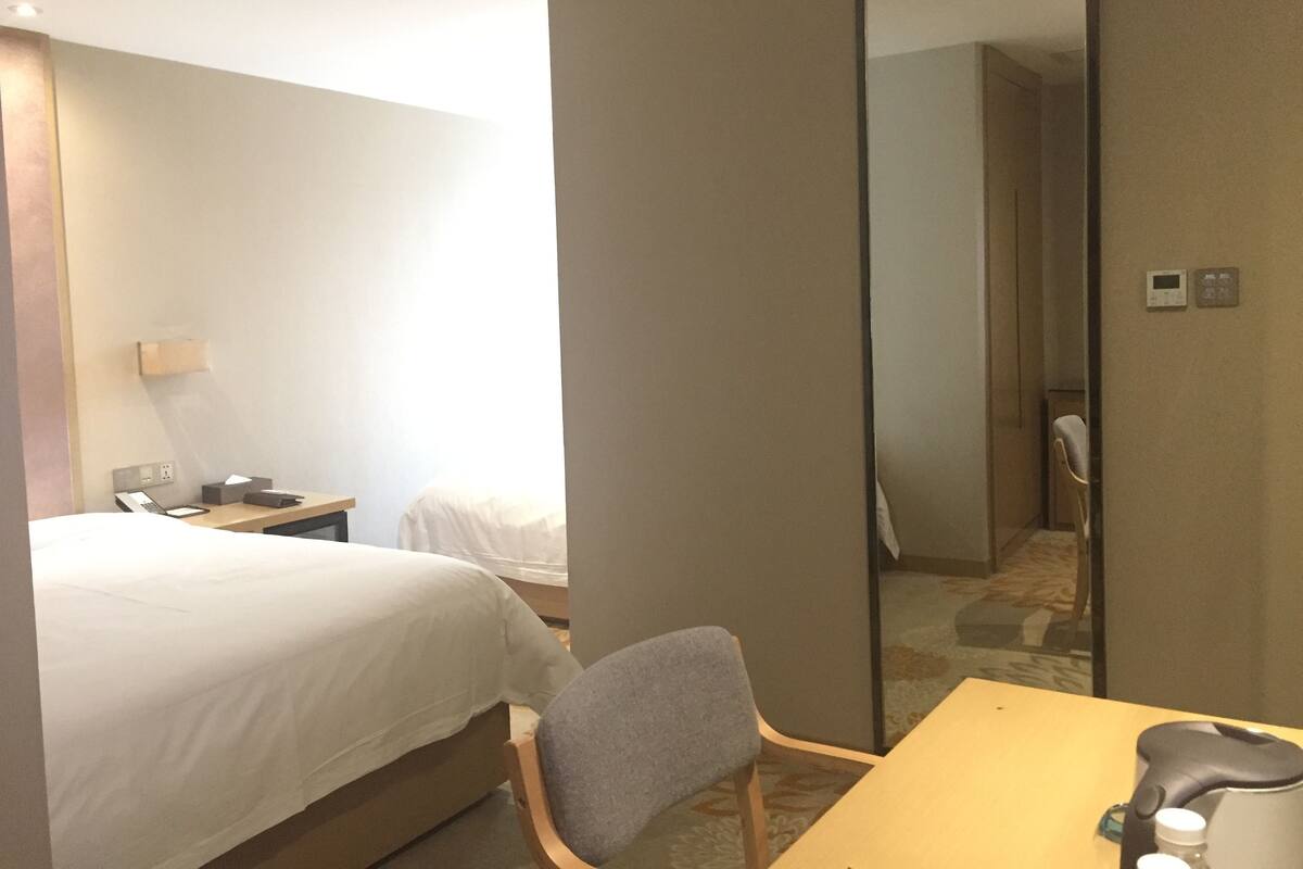 Ett hotellrum med en säng, ett skrivbord, en stol, en spegel och ett nattduksbord med en lampa.