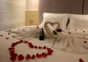 Una cama con pétalos de rosa formando un corazón, una botella y dos almohadas con forma de cisne.