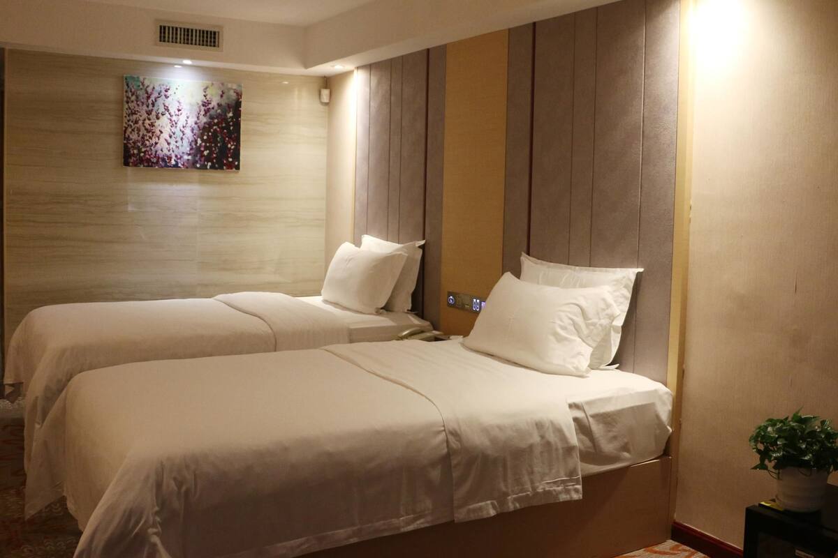 Ein Hotelzimmer mit zwei Betten, einem großen abstrakten Gemälde an der Wand und einer Zimmerpflanze auf einem Beistelltisch.