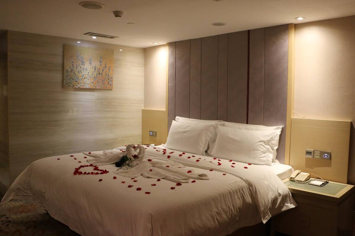 Ein Hotelzimmer mit einem ordentlich bezogenen Bett, einem Nachttischtelefon und einem an der Wand hängenden Kunstwerk.