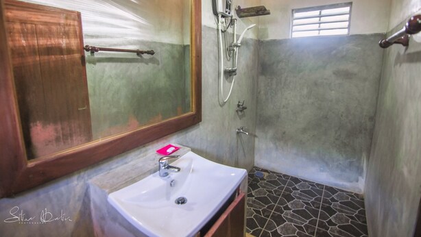 A bathroom with a white sink, a wooden-framed mirror, a shower with a handheld showerhead, and a small window. - 360 Rainforest (Deniyaya)