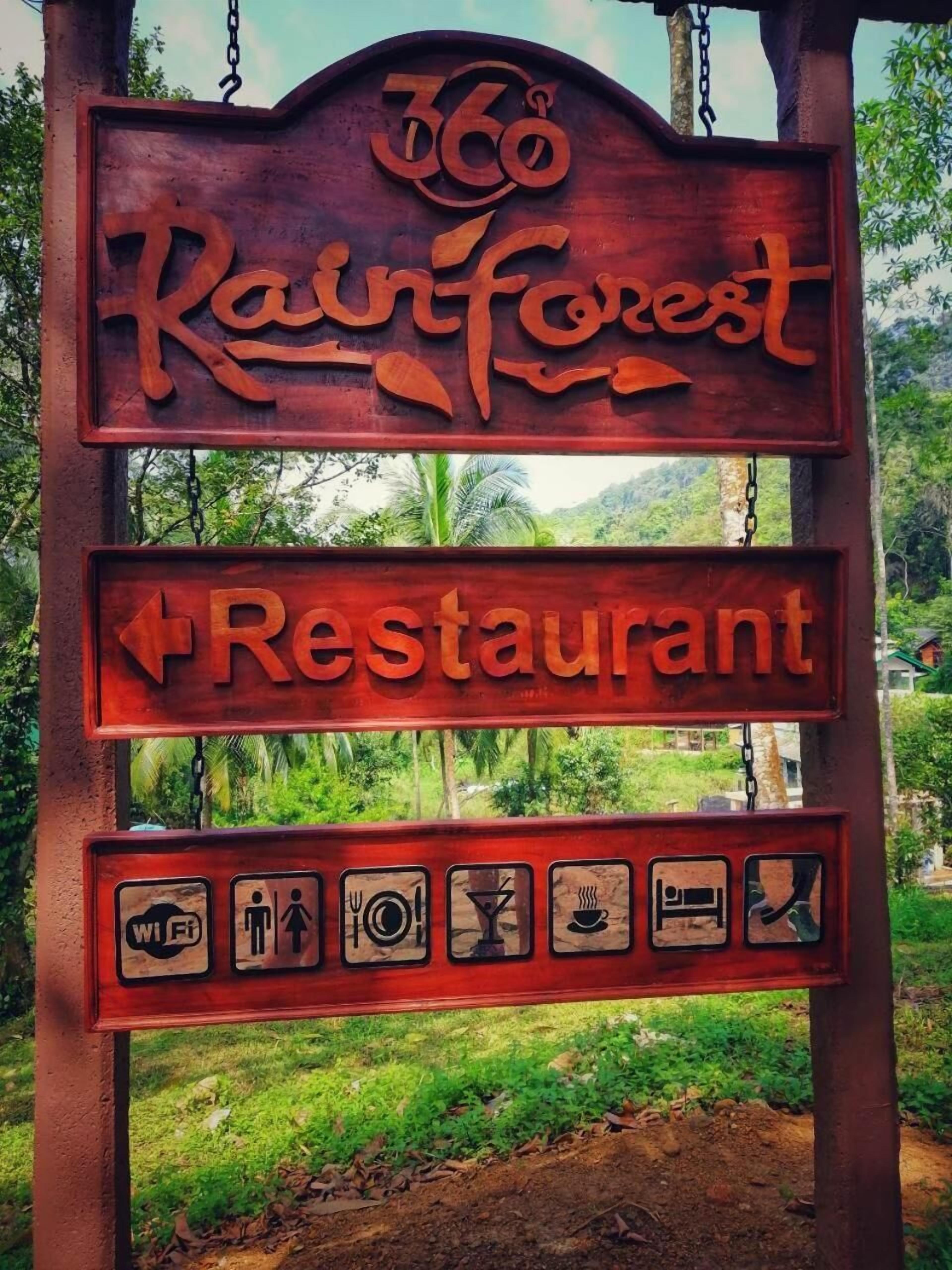 En träskylt för restaurangen Rainforest, med pilar som visar vägen och ikoner som anger var man hittar Wi-Fi, toaletter och andra bekvämligheter.