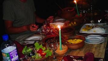 Une table à manger dressée pour un repas, avec différents plats, une bougie et une bouteille d’eau.