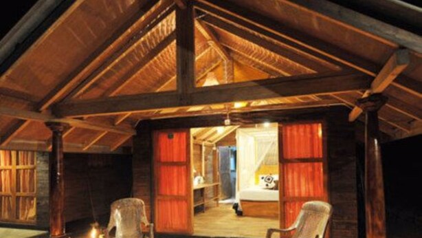 A rustic cabin with a wooden exterior, a porch with two chairs, and a visible bedroom with a bed and nightstand. - 360 Rainforest (Deniyaya)