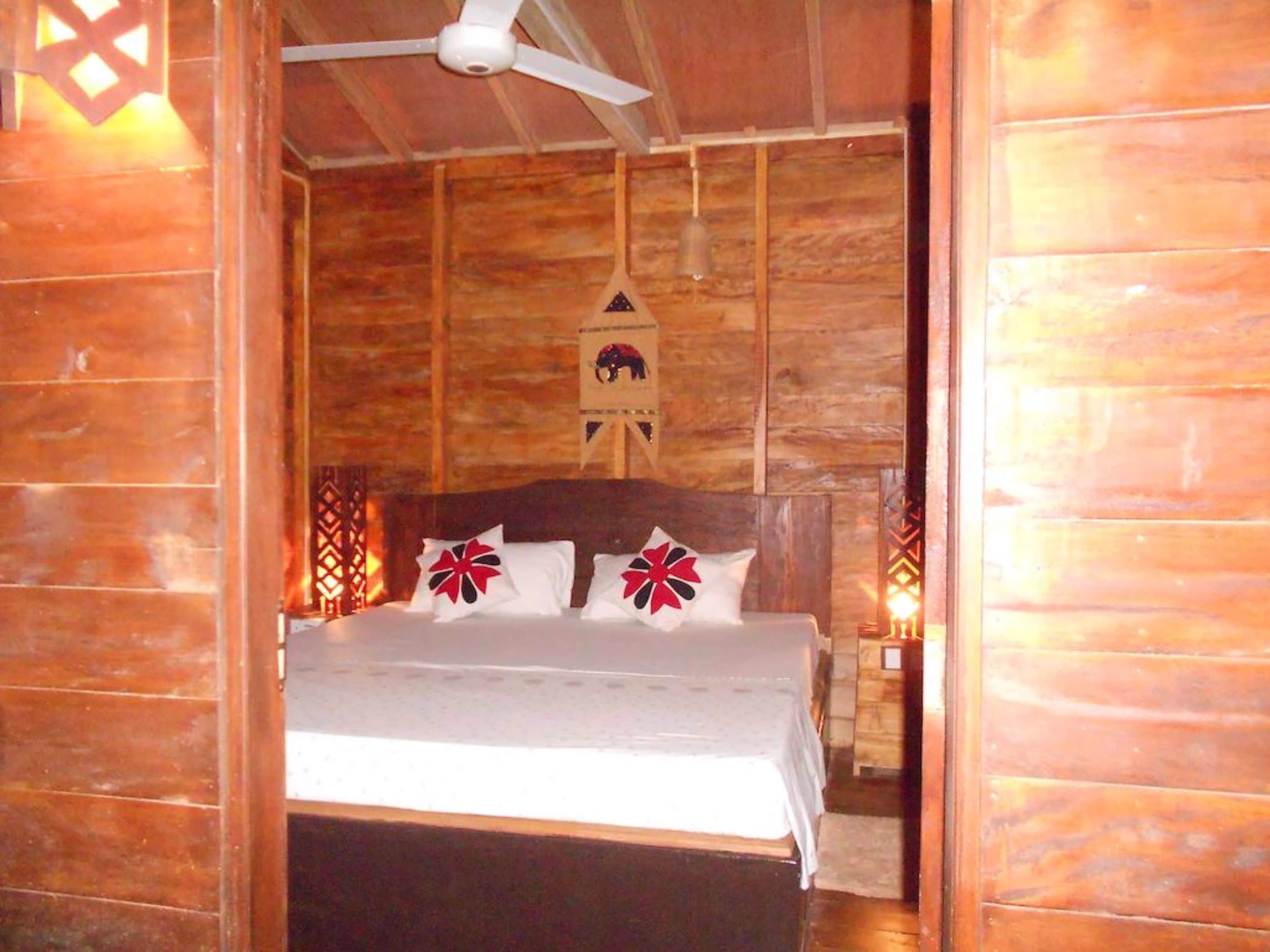 Una habitación de madera con una cama, un ventilador de techo y un reloj en la pared.