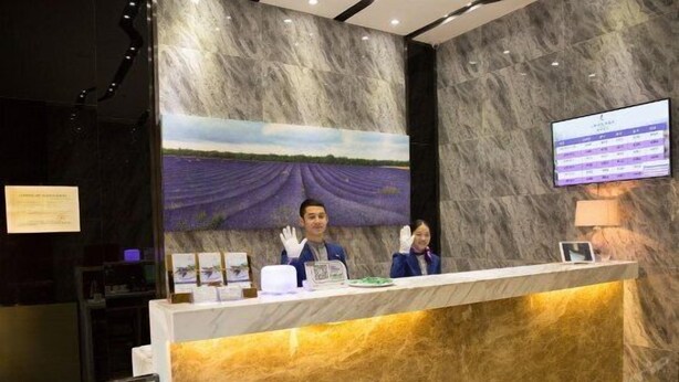A reception desk with a marble wall backdrop, a television screen, and a framed landscape painting. - Lavande Hotel (Guangzhou)