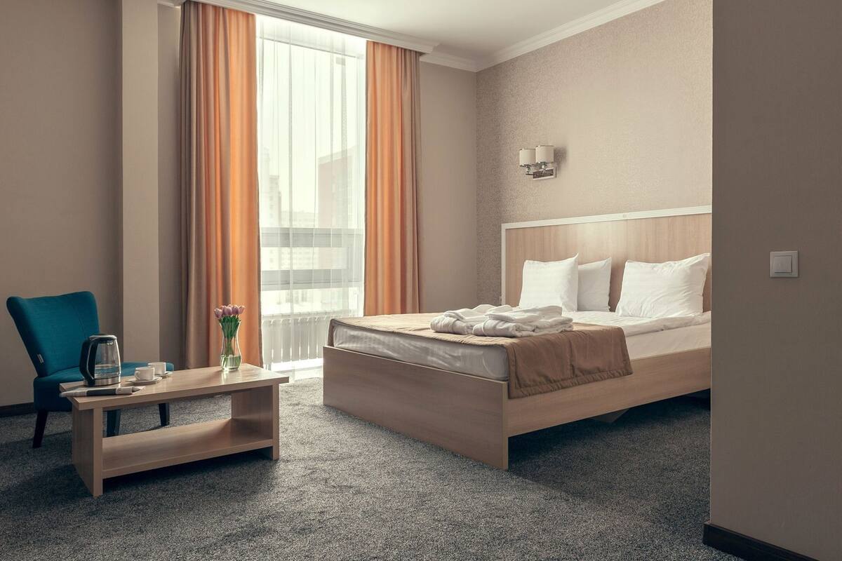 Habitación de hotel con cama, una mesita de centro, una silla y ventana con cortinas.