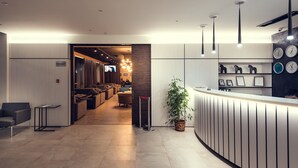 A modern reception area with a wooden reception desk, a seating area with sofas, and a television in the background. - AyKun Hotel (Astana)