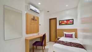 Quarto de hotel com cama, escrivaninha, cadeira, guarda-roupa e ar condicionado fixado na parede.