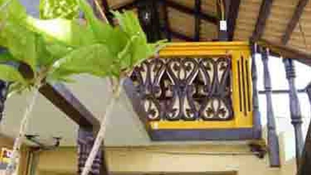 Ein Gebäude im traditionellen Baustil, mit einem Balkon, der kunstvoll gestaltete Metallgeländer und eine Holzbalkendecke aufweist.
