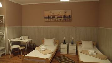 Una habitación de hotel con dos camas individuales, una mesita pequeña, una silla, una mesita de noche y una lámpara.