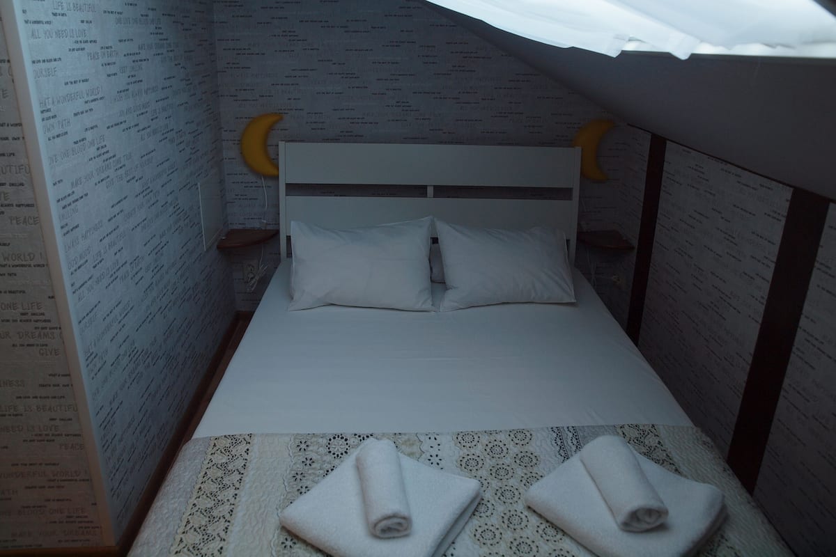 A small, narrow room with a single bed, a headboard with a crescent moon design, and a patterned wall.