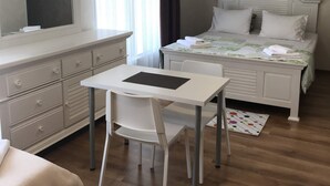 Un dormitorio con cama, mesita de noche, una silla, escritorio y ventana con cortinas.