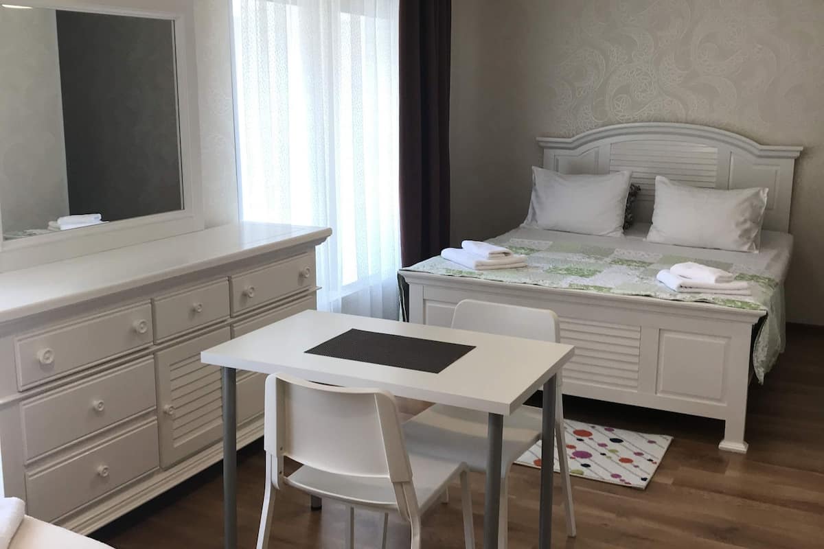 A bedroom with a bed, a bedside table, a chair, a desk, and a window with curtains.
