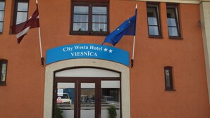 Entrada del Hotel City Westa con un cartel, dos banderas y plantas en macetas.