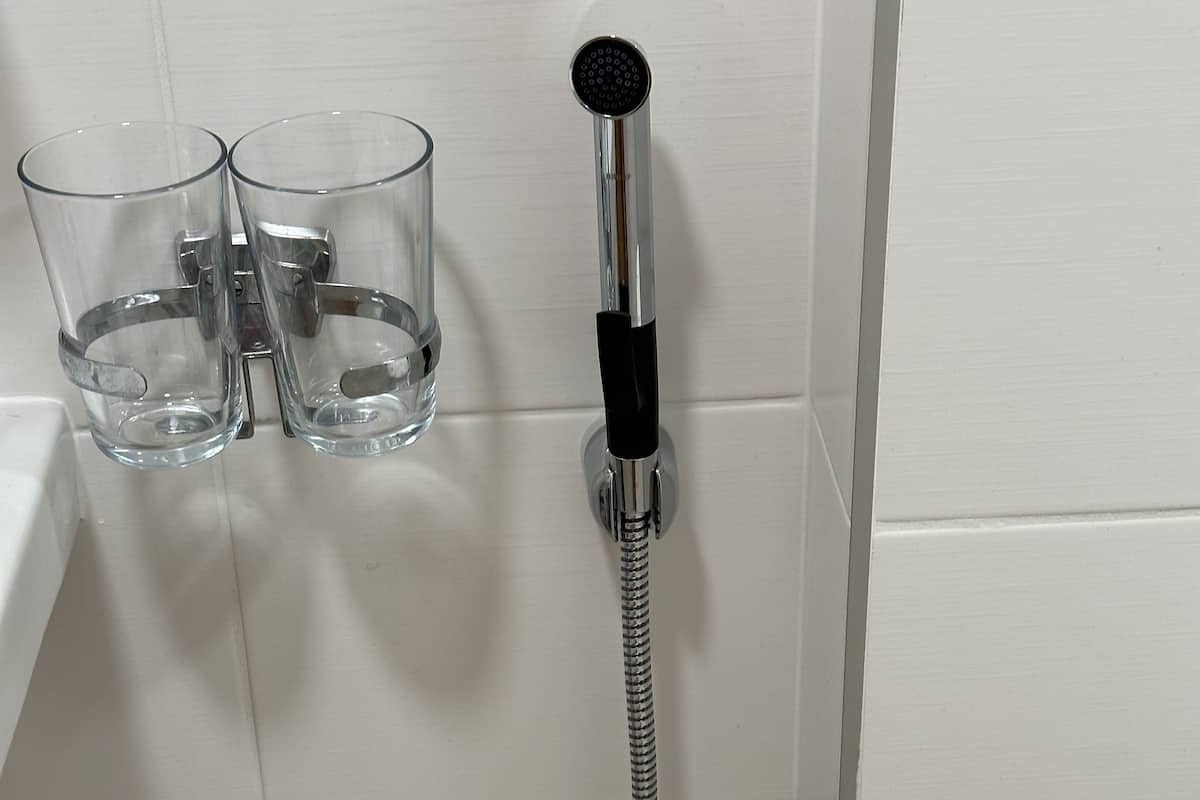 Ducha con un cabezal de mano y dos vasos transparentes en una pared de azulejos blancos.