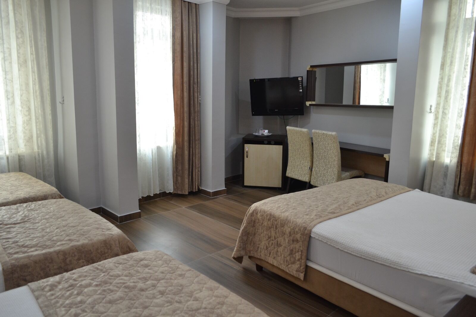 Habitación de hotel con dos camas, televisor, escritorio y espejo.