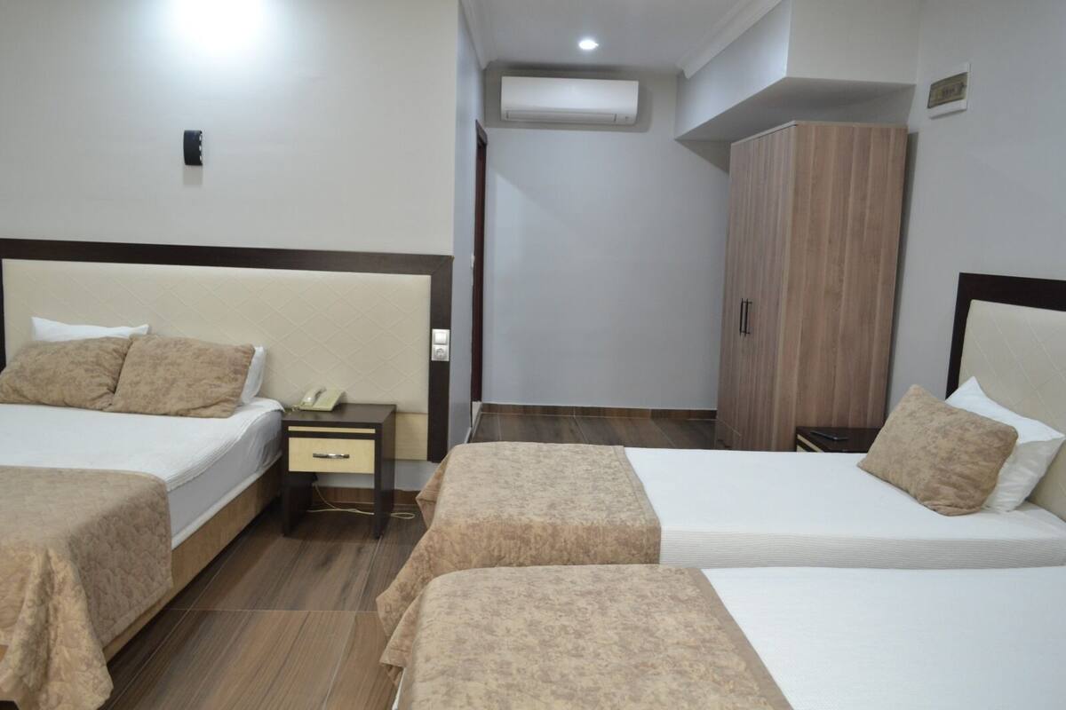 A hotel room with two beds, a bedside table with a phone, a wardrobe, and an air conditioning unit.