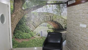 A reception area with a mural of a tree and bridge, a black leather chair, and a brick wall.