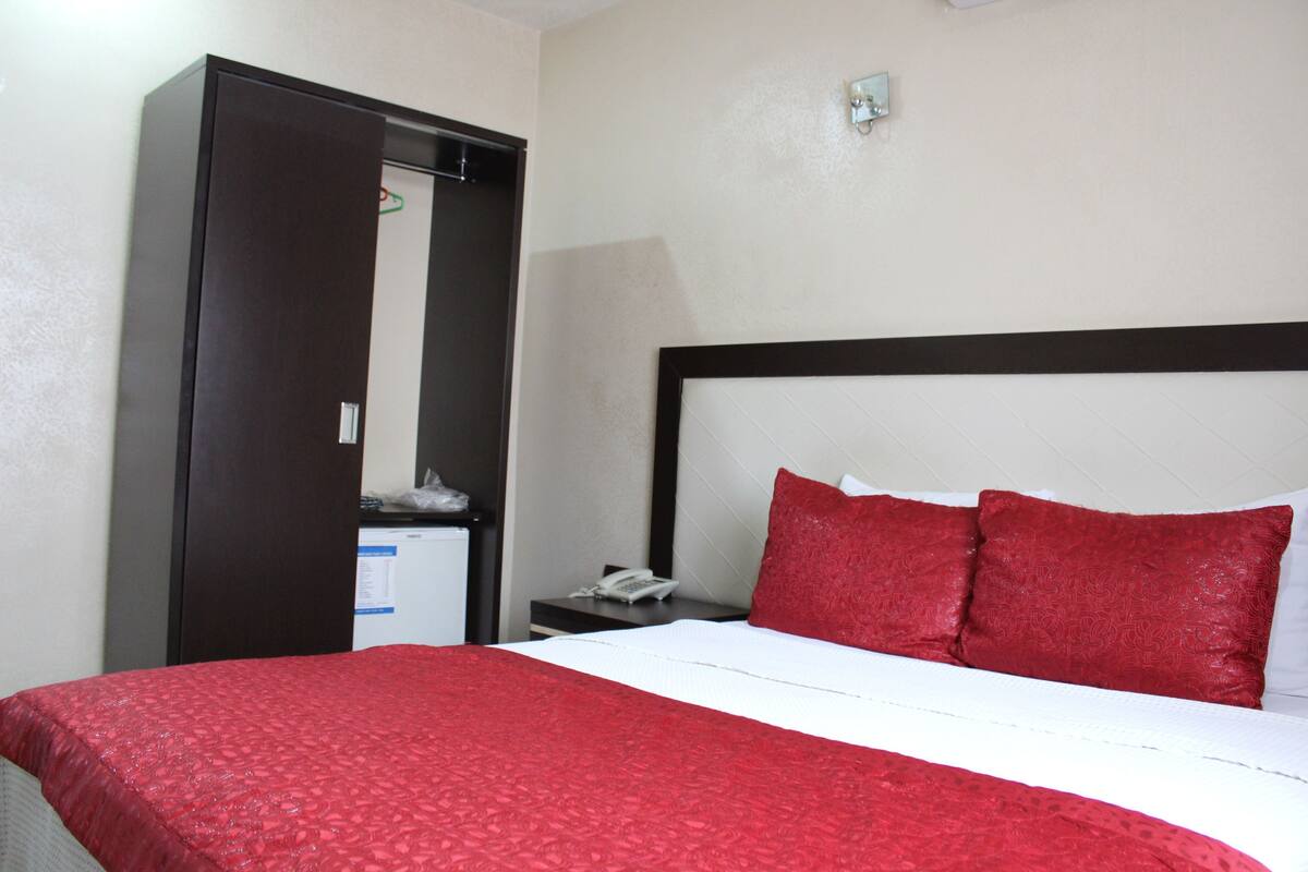 A hotel room with a bed, a wardrobe, a nightstand, and a desk.