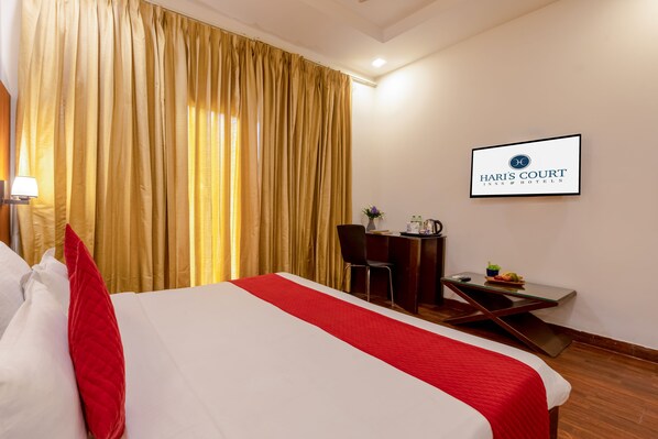 A hotel room with a bed, a desk, a chair, a table with a coffee pot, and a sign on the wall.