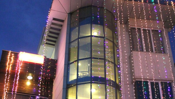 A modern building with a curved glass facade and string lights.