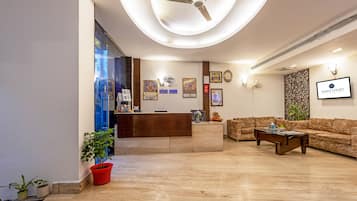 A hotel reception area with a reception desk, a sofa, and a ceiling fan.