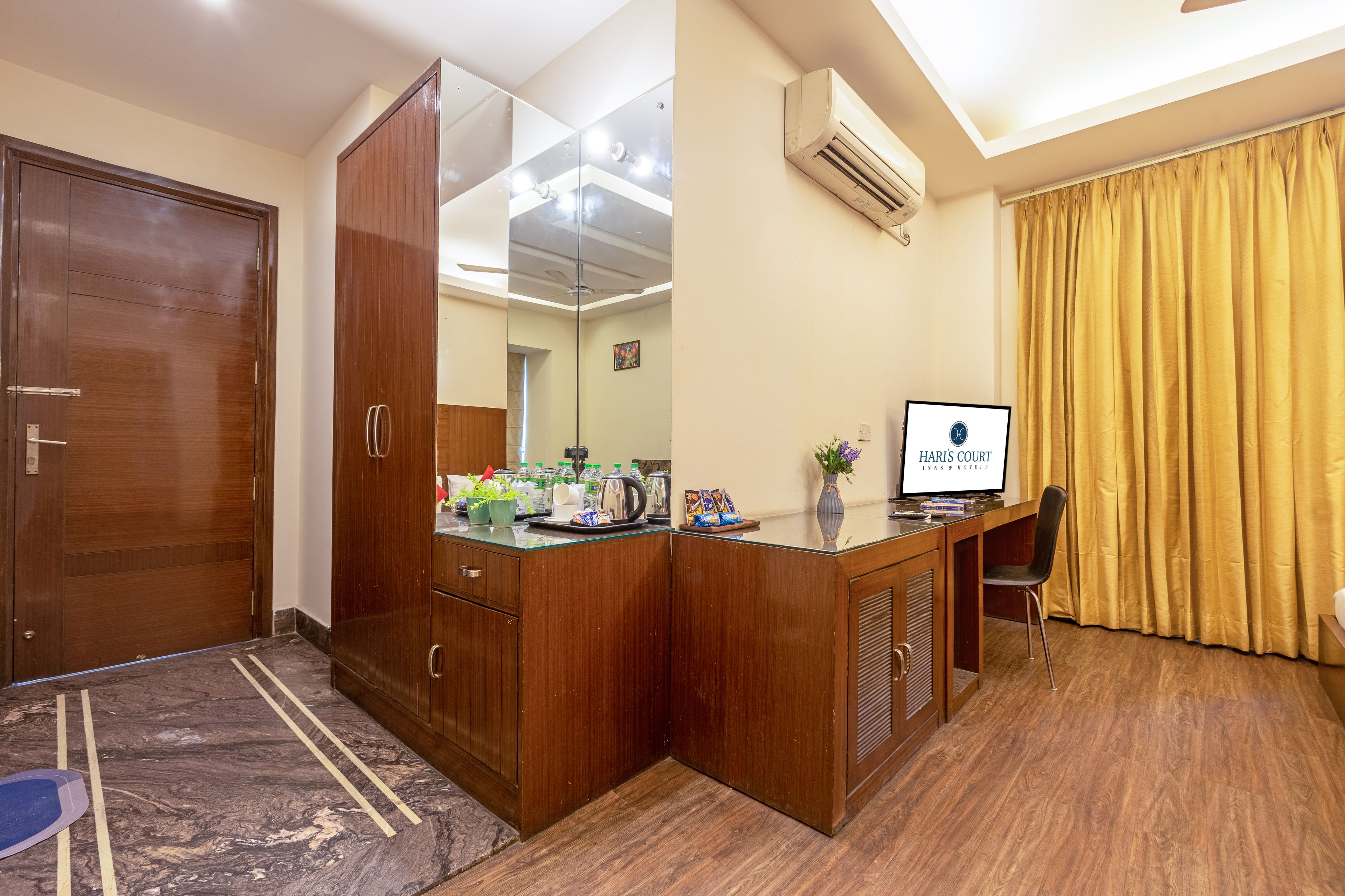 A hotel room with a wooden wardrobe, a desk with a computer, a coffee maker, and a window with curtains.
