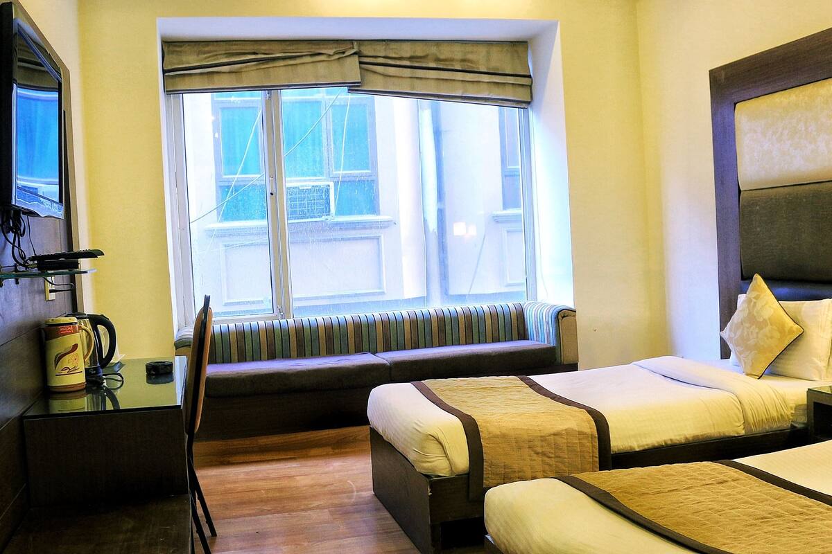 Une chambre d’hôtel avec deux lits, une fenêtre donnant sur un paysage agréable, un radiateur et un bureau équipé d’une bouilloire et d’une tasse.