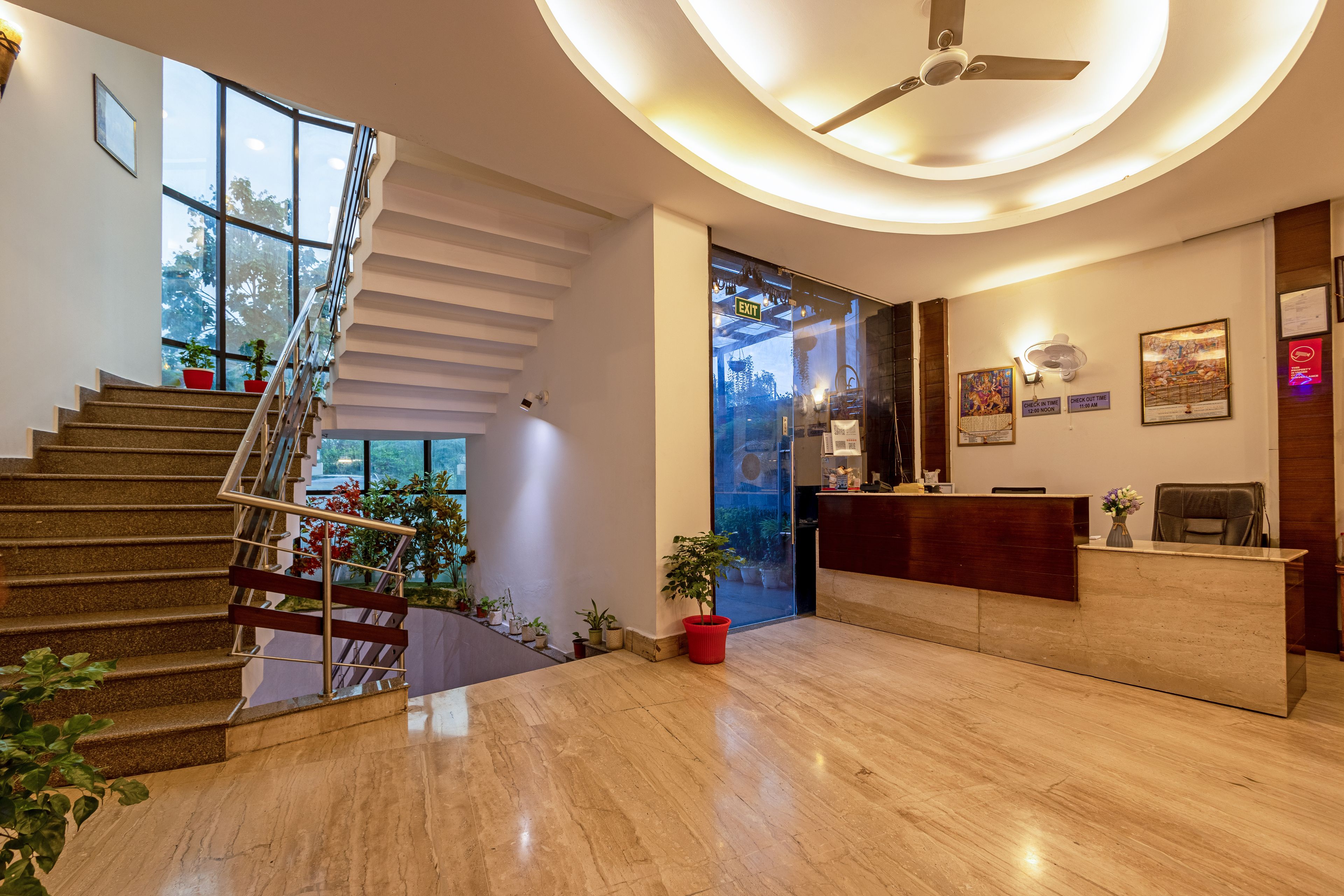 A hotel lobby with a staircase, reception desk, and a ceiling fan.
