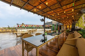 Een terras met rieten meubels en een glazen tafel, met uitzicht op een stadsgezicht.