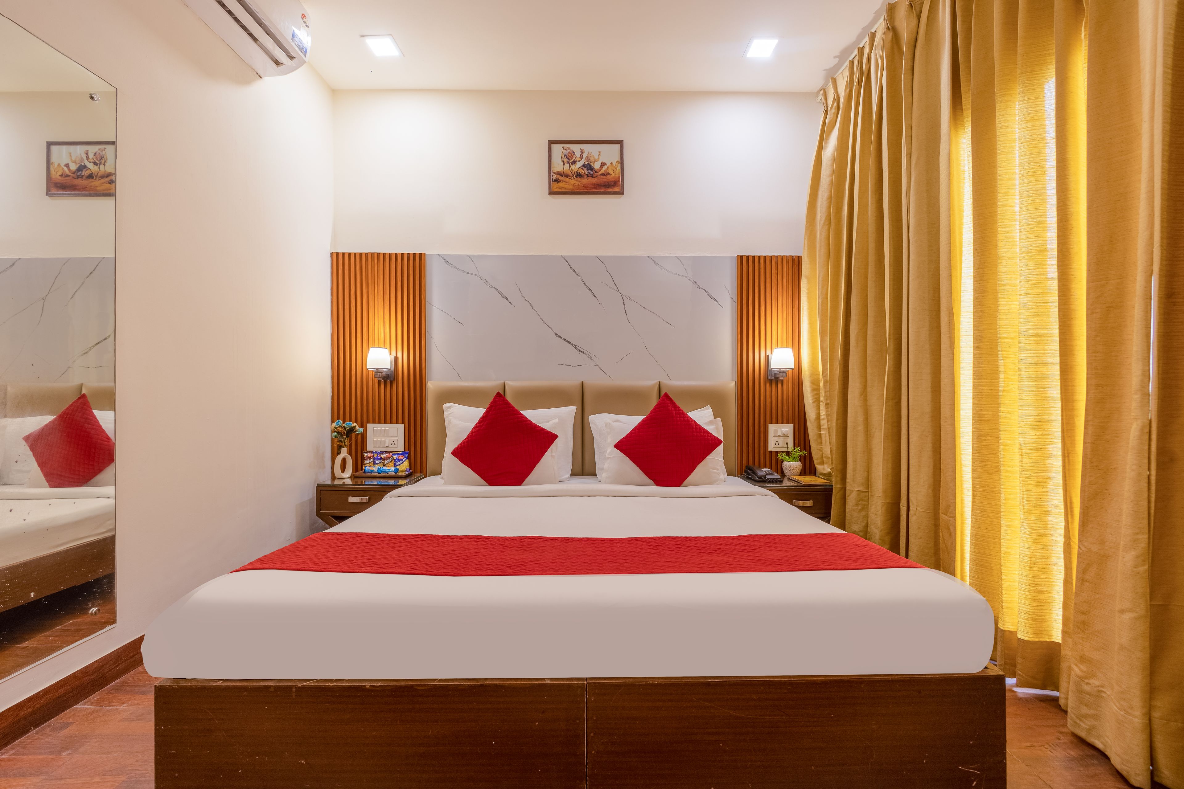 A hotel room with a large bed, a nightstand, a mirror, and a window with curtains.