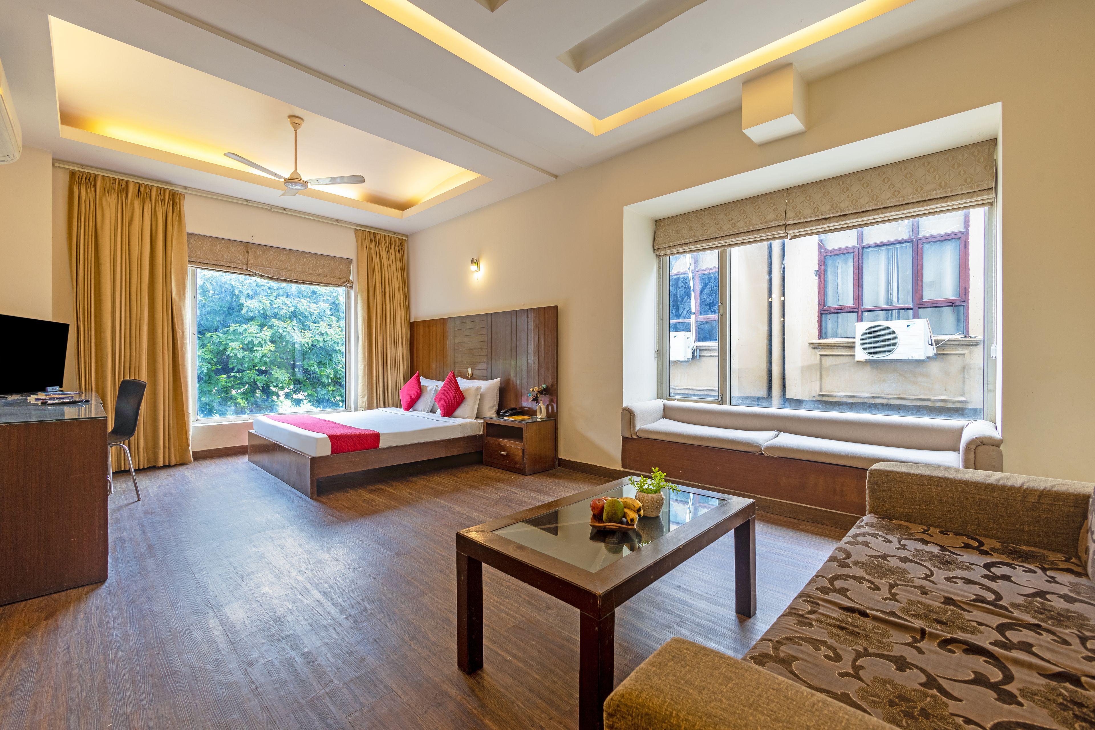 A hotel room with a bed, a sofa, a coffee table, a desk, and a window with a view of trees.