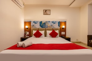 A hotel room with a large bed, red and white bedding, two nightstands with lamps, a painting on the wall, and a red throw blanket.